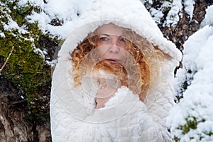 Portrait of redhead mature woman in her fifties with red curly hair with hooded coat freezes in the snowy winter landscape