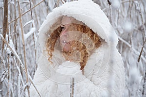 Portrait of redhead, mature woman in her fifties with snowflakes on red curly hair, with hooded coat, freezes in the snowy winter