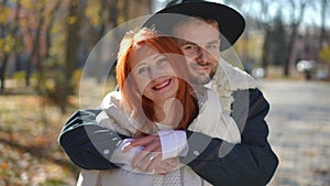 Portrait of redhead mature woman looking at camera smiling as adult man walking from background hugging. Happy confident