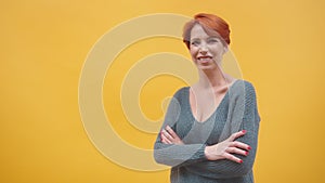 Portrait of redhead middle aged woman with crosed hands smilling, isolated on the orange background