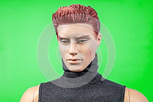 Portrait of redhead serious male plastic mannequin in dark turtleneck isolated on green background, close up.