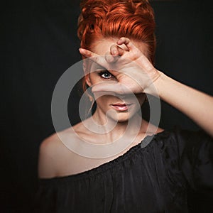 Portrait of redhead woman with blue eyes. Girl looks directly into the camera through her fingers.