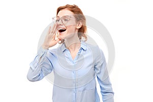 Portrait of redhead young woman screaming into her palms on white studio background. Important information