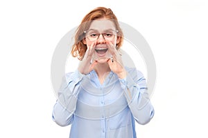 Portrait of redhead young woman screaming into her palms on white studio background. Important information