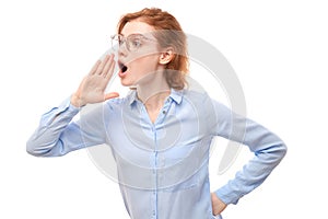 Portrait of redhead young woman screaming into her palms on white studio background. Important information