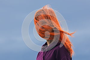 Portrait of redheaded young woman with blowing hair against blue cloud