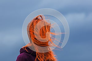 Portrait of redheaded young woman with blowing hair against blue cloud