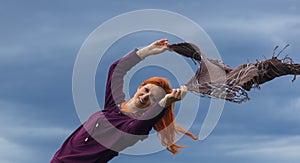 Portrait of redheaded young woman playing with blowing scarf in wind against blue cloud