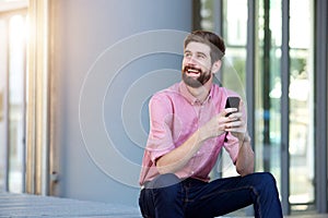 Relaxed man with beard sitting outside with cellphone