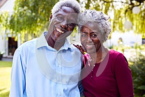 Portrait Of Relaxed Senior Couple Standing In Garden At Home After Retirement