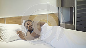 Portrait of relaxed young African American man waking up in the morning at home. Carefree handsome guy lying in white