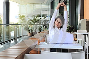 Portrait of relaxed young Asian business woman sitting and raising hands over head in office.