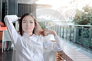 Portrait of relaxed young Asian business woman sitting and touch head with hands in office. Sunshine effect.