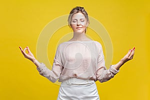 Portrait of relaxed young beautiful woman with blonde hair in casual beige blouse, isolated on yellow background