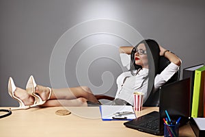 Portrait of a relaxed young businesswoman sitting with legs on d