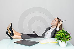 Portrait of a relaxed young businesswoman holding phone sitting with legs on desk in a office