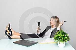 Portrait of a relaxed young businesswoman holding phone sitting with legs on desk in a office