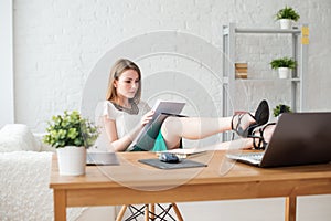 Portrait of a relaxed young businesswoman sitting with legs on desk in office.