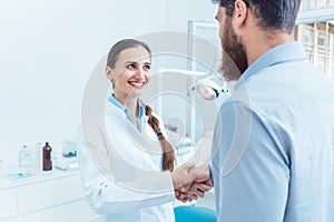 Portrait of a reliable and cheerful dentist shaking the hand of a patient