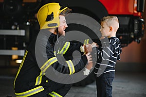 Portrait of rescued little boy with firefighter man standing near fire truck. Firefighter in fire fighting operation.