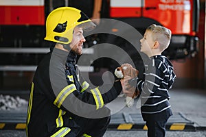 Portrait of rescued little boy with firefighter man standing near fire truck. Firefighter in fire fighting operation.