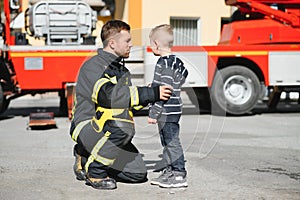 Portrait of rescued little boy with firefighter man standing near fire truck. Firefighter in fire fighting operation.