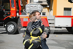 Portrait of rescued little boy with firefighter man standing near fire truck. Firefighter in fire fighting operation.