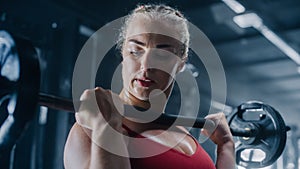 Portrait of a Resolute Female Athlete Defyingly Exercising with Weights on a Barbell in a Gym. Close