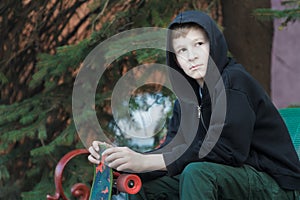 Portrait of resting teenage boy holding skateboard and sitting on park bench