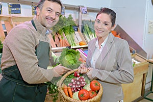 Portrait retailer and customer holding basket fresh vegetables