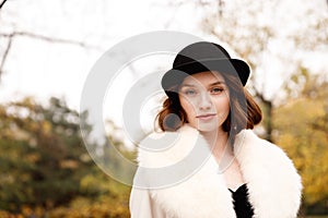 Portrait of retro girl in black hat, fur coat and black gloves in autumn park