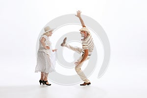 Portrait of retro style dancers, senior man and woman in vintage attire dancing swing  on white background
