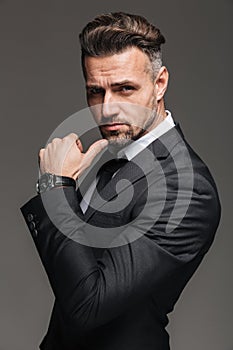 Portrait of rich brunette man 30s in black suit posing on camera