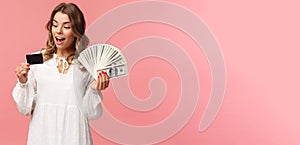 Portrait of rich good-looking blond girl in white dress, holding dollars money and credit card, winning lottery, think
