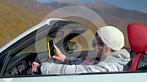 portrait of rich successful young man in his lux cabrio car on mountain road, trip in highland