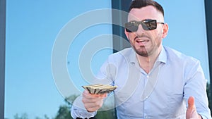 Portrait of a rich young successful man in sunglasses showing a pile of money.