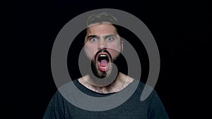 Portrait of roar handsome man with beard standing and screaming with big open mouth, isolated on black background. Young