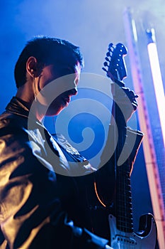 Portrait of rockstar performer playing at electric guitar adjusting sound before rock concert