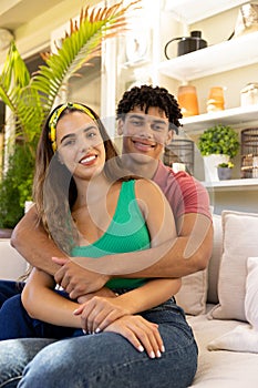 Portrait of romantic biracial young man embracing girlfriend while sitting on sofa in living room