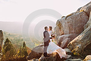 Portrait of romantic newlywed couple kiss in sunset lights on majestic mountain landscape with big rocks as backround