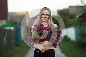 Portrait of a romantic smiling young woman with a bouquet of lilac outdoors shallow depth of field