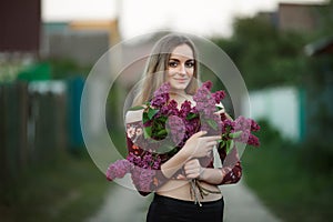 Portrait of a romantic smiling young woman with a bouquet of lilac outdoors shallow depth of field