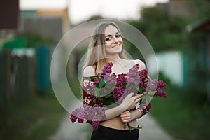 Portrait of a romantic smiling young woman with a bouquet of lilac outdoors shallow depth of field