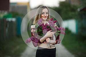 Portrait of a romantic smiling young woman with a bouquet of lilac outdoors shallow depth of field