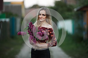 Portrait of a romantic smiling young woman with a bouquet of lilac outdoors shallow depth of field