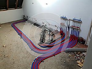 A portrait of a room under construction with a central heating collector on the wall. The warm and cold water tubes are running