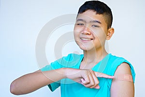 Portrait of rural Asian boy standing against white background looking camera smiling happily pointing at plaster on his arm after