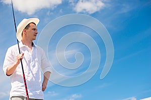 Portrait of a rural fisherman with a fishing rod in a hat on a b