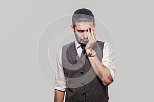 Portrait of sad alone depressed handsome bearded brunette man in white shirt and waistcoat standing, holding head down, touching