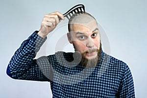 Portrait of sad bearded bald guy holding a comb in his hand. The concept of hair loss and hair transplantation